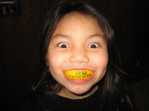 A smiling Asian girl with a citrus fruit in her mouth